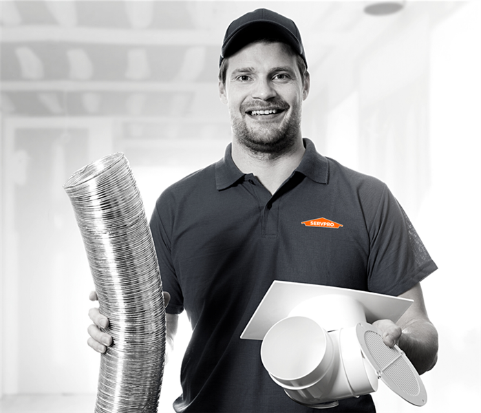 black and white image of a servpro technician staring at the camera holding HVAC parts