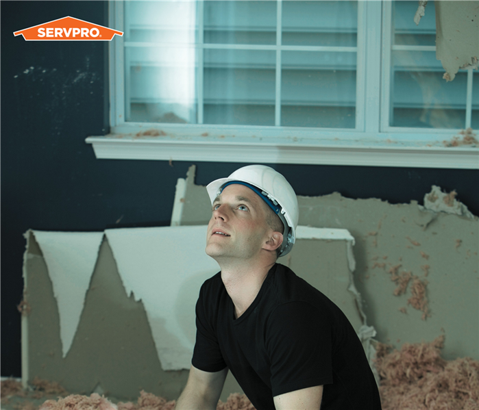 SERVPRO production technician squatting near the ground looking up at the ceiling, wearing a hard helmet, exposed walls