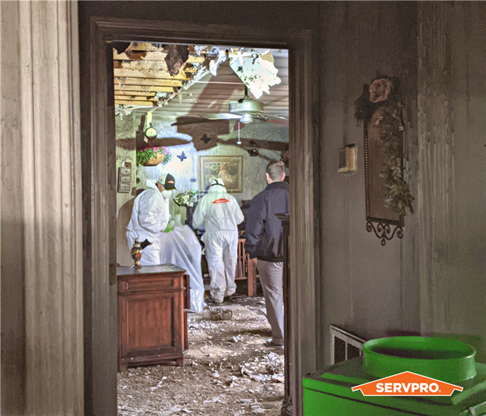 men in hazmat suits cleaning after a fire near me, servpro techs, in a fire damaged home through a doorway