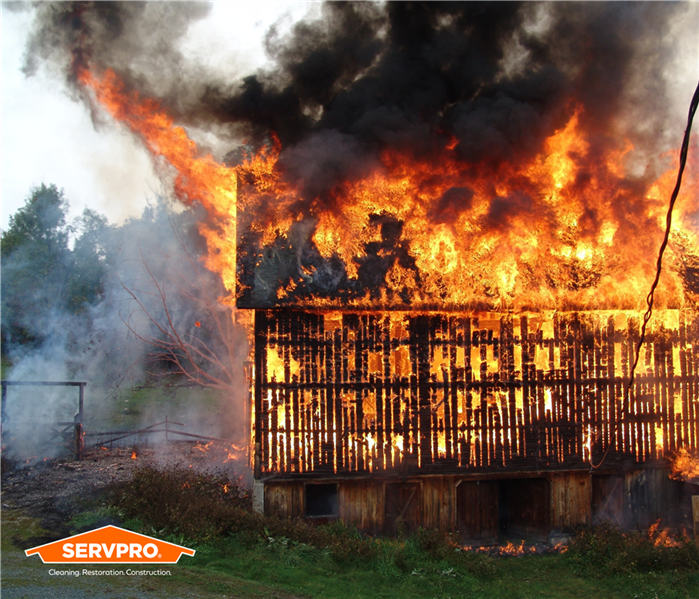 barn type building caught on fire, flames soar above it, wood slats visible